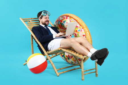 Man with laptop in deck chair on light blue backgroundの写真素材