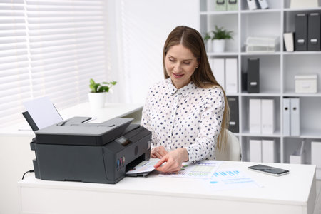 Woman using printer at desk near window in office