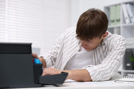 Man checking printer ink levels at white desk in office