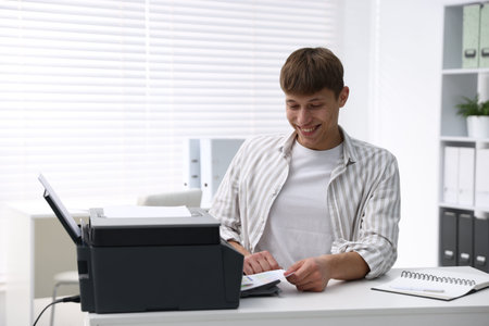 Smiling man working with printer at white desk in office