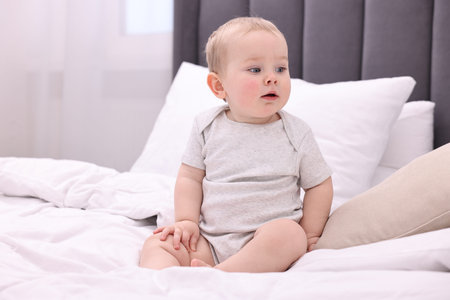 Cute little baby sitting on bed at home