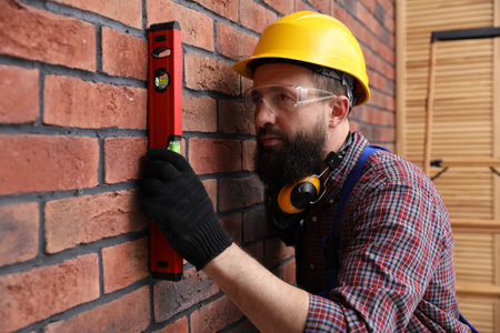 Worker measuring wall with building level indoors