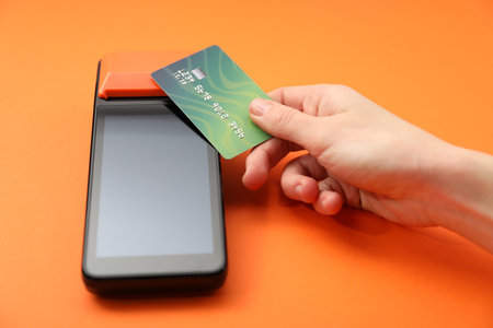 Woman with credit card using payment terminal on orange background, closeup