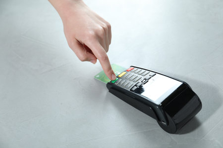 Woman with credit card using payment terminal at light grey table, closeup. Space for text