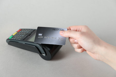 Woman with credit card using payment terminal on light grey background, closeup