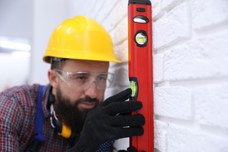 Worker measuring wall with building level indoors
