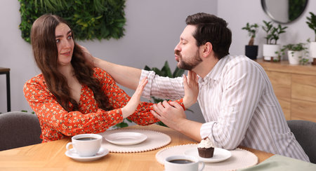 Embarrassed woman refusing kiss from man at table during dinner indoorsの写真素材