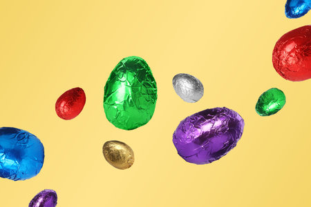Sweet chocolate eggs in shiny foil flying on pastel orange background