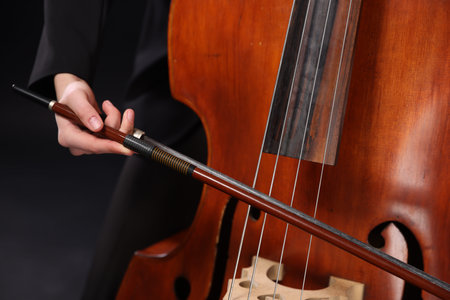 Girl playing double bass on black background, closeup