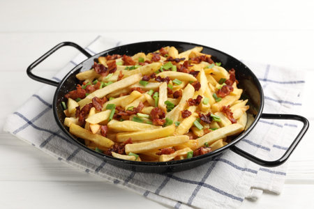 Delicious French fries with bacon and green onion on white wooden table, closeup