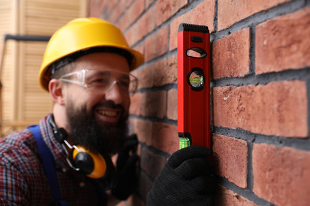 Worker measuring wall with building level indoors, selective focus
