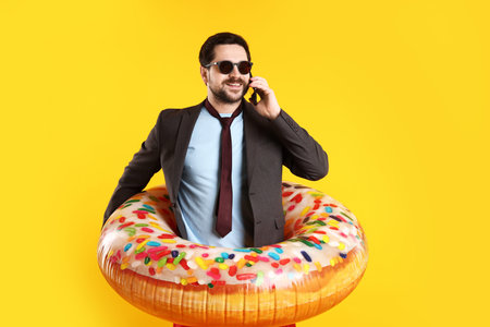 Office worker with inflatable ring talking on smartphone against orange backgroundの写真素材