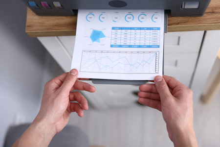 Man taking printed sheet of paper from printer at chest of drawers, above view