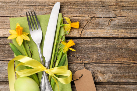 Easter table setting. Beautiful silverware floral decor and painted egg on wooden background, top...