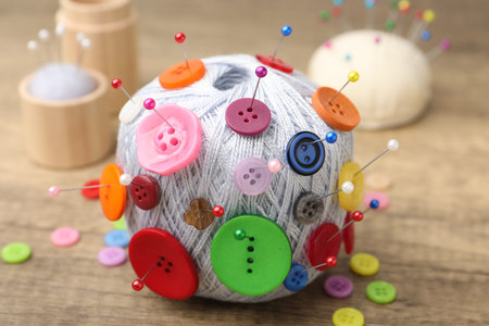 Skein of yarn with buttons and pins on wooden table, closeup