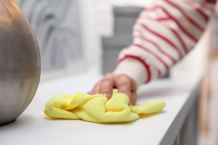 Woman wiping cabinet with microfiber cloth at home, closeup