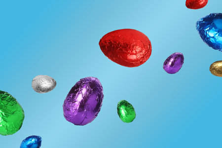 Sweet chocolate eggs in shiny foil flying on pastel blue background