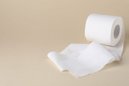 Roll of toilet paper on beige background, closeup. Space for text