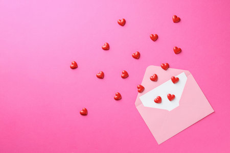 Envelope with greeting card and decorative hearts on pink background, flat lay. Space for textの写真素材