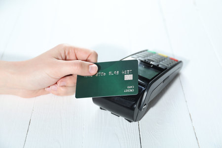 Woman with credit card using payment terminal at white wooden table, closeup