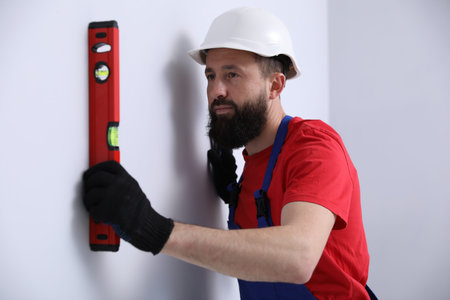 Worker measuring wall with building level indoors