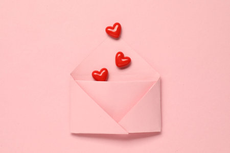 Love. Envelope with red decorative hearts on pink background, flat lay