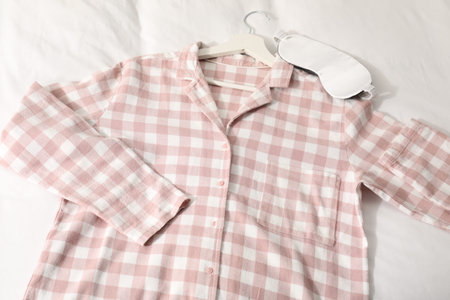 Stylish pyjama shirt and sleeping mask on bed, above view