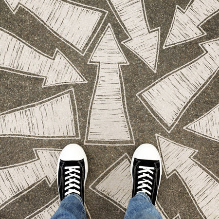 Man in sneakers standing on road with arrows pointing in different directions, top view. Start your...
