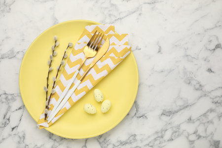 Easter celebration. Festive setting with cutlery, willow branches and painted eggs on white marble...