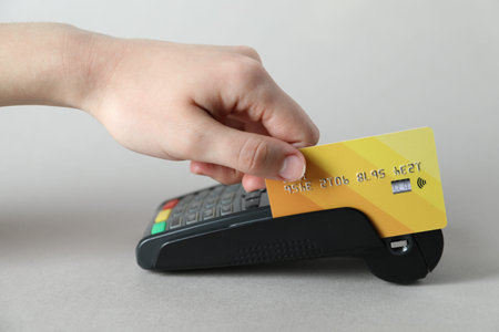 Woman with credit card using payment terminal on light grey background, closeup