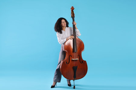 Woman playing double bass on light blue background