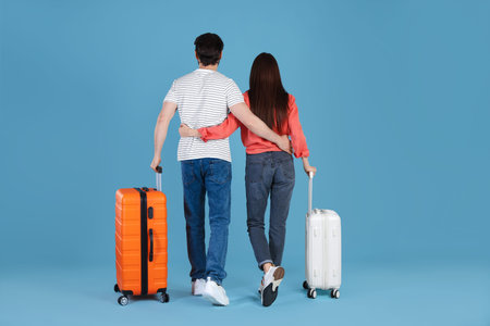 Couple with suitcases on light blue background, back view