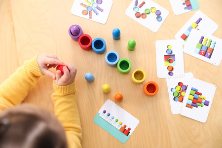 Cute little girl playing with toys at wooden table indoors, above view