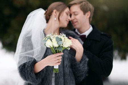 Happy newlywed couple with bouquet of flowers outdoors on winter day, selective focusの写真素材