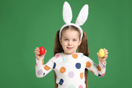 Easter celebration. Portrait of smiling little girl in headband with bunny ears holding painted eggs...