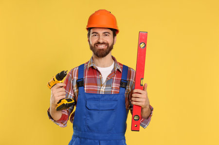 Professional builder with level tool and screw gun on yellow background