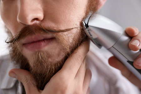 Handsome man trimming his beard at home, closeup