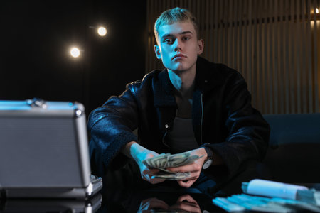 Young businessman in jacket with dollar banknotes in dark room