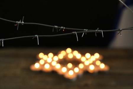 Holocaust Remembrance Day. Barbed wire and burning candles in shape of Star of David on table...