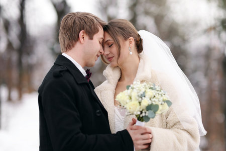Happy newlywed couple with bouquet of flowers outdoors on winter dayの写真素材