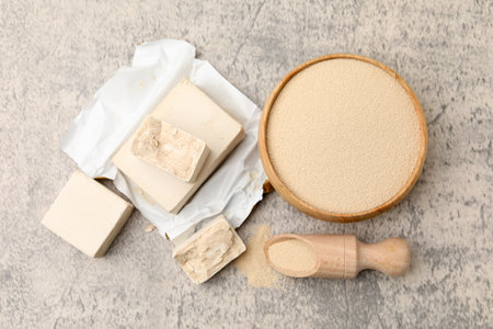 Pieces of fresh, dried yeast, scoop and bowl on grey textured table, flat layの写真素材