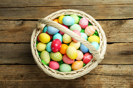Easter basket with painted eggs on wooden table, top view