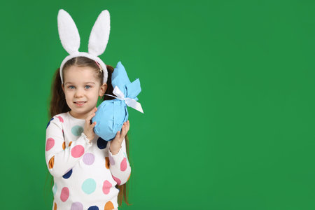 Easter celebration. Portrait of smiling little girl in headband with bunny ears holding wrapped gift...