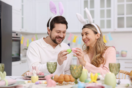 Easter celebration. Happy couple with painted eggs at served table in kitchen