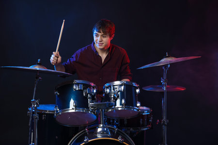 Teenage boy learning how to play drums in color light against dark backgroundの写真素材
