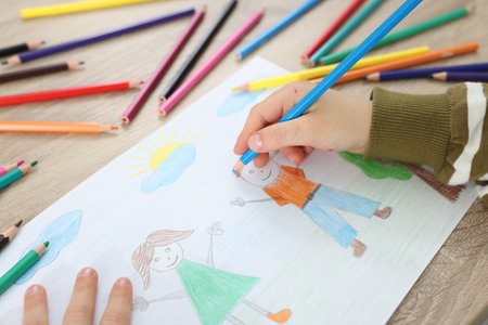 Little boy drawing with pencil at wooden table, closeup