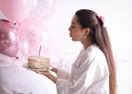 Birthday celebration. Beautiful woman blowing candle on delicious cake at home