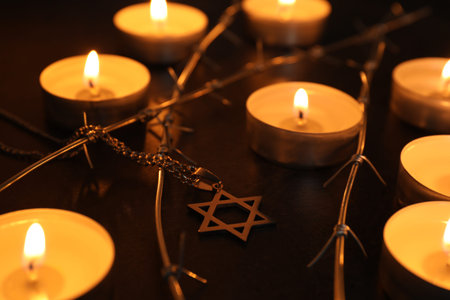 Holocaust Remembrance Day. Burning candles, pendant in shape of Star of David and barbed wire on...