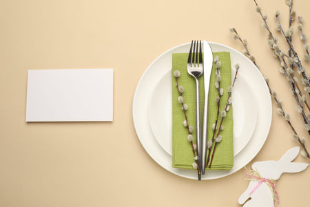 Easter celebration. Festive table setting with willow branches, blank card and cutlery on beige...