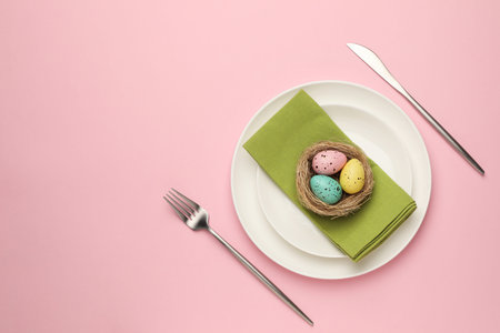 Easter celebration. Festive table setting with painted eggs and cutlery on pink background, flat lay...